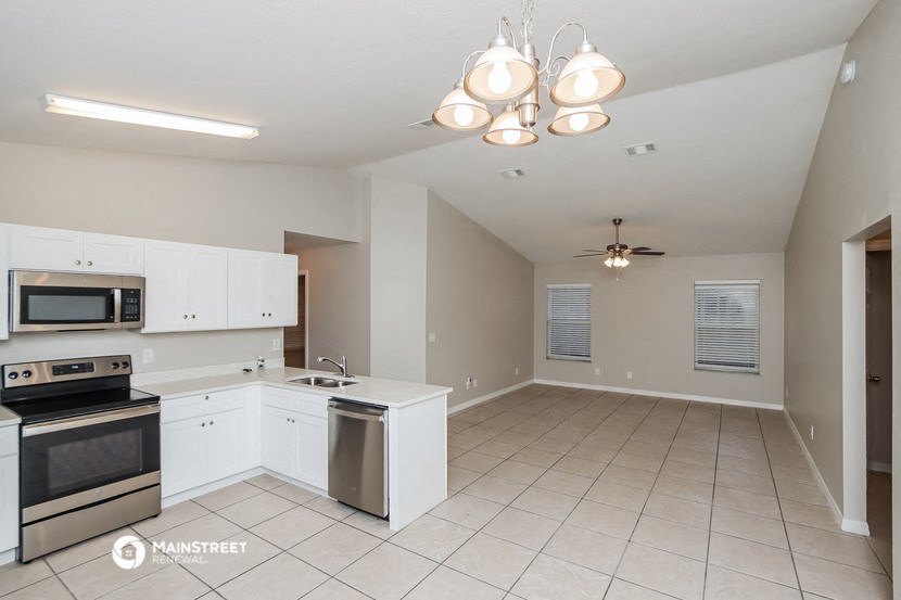 an empty kitchen with white cabinets and appliances and a ceiling fan