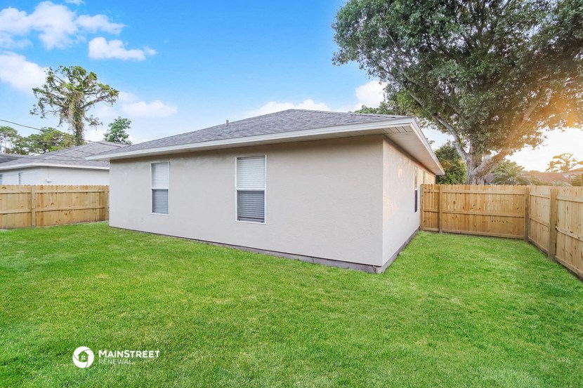 a backyard with a small white house and a wooden fence