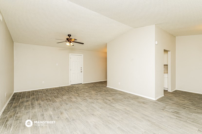 the spacious living room with wood flooring and a ceiling fan