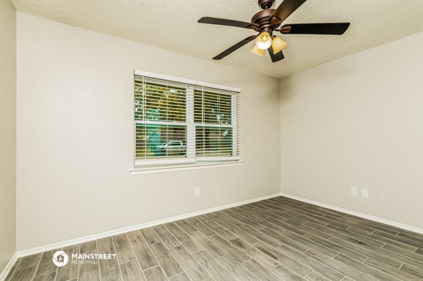 the spacious living room with a large window and a ceiling fan