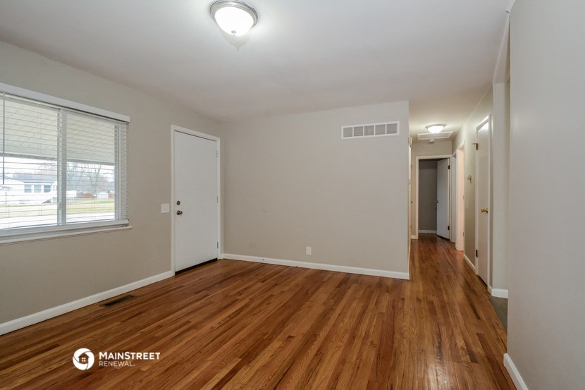 the living room of an apartment with wood flooring and a large window