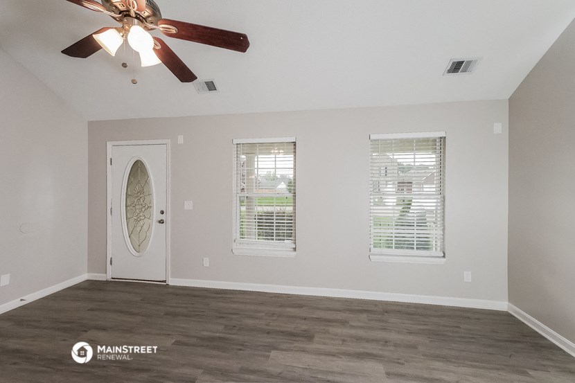 an empty living room with a ceiling fan and three windows