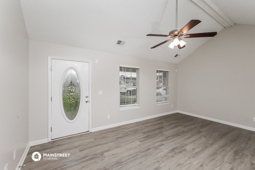 the living room of an empty home with a ceiling fan and a door to a