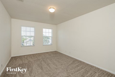 a spacious living room with carpet and two windows