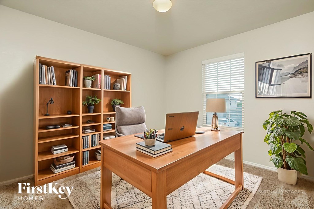 A room with a desk, a laptop, a chair, a bookshelf, and a potted plant.