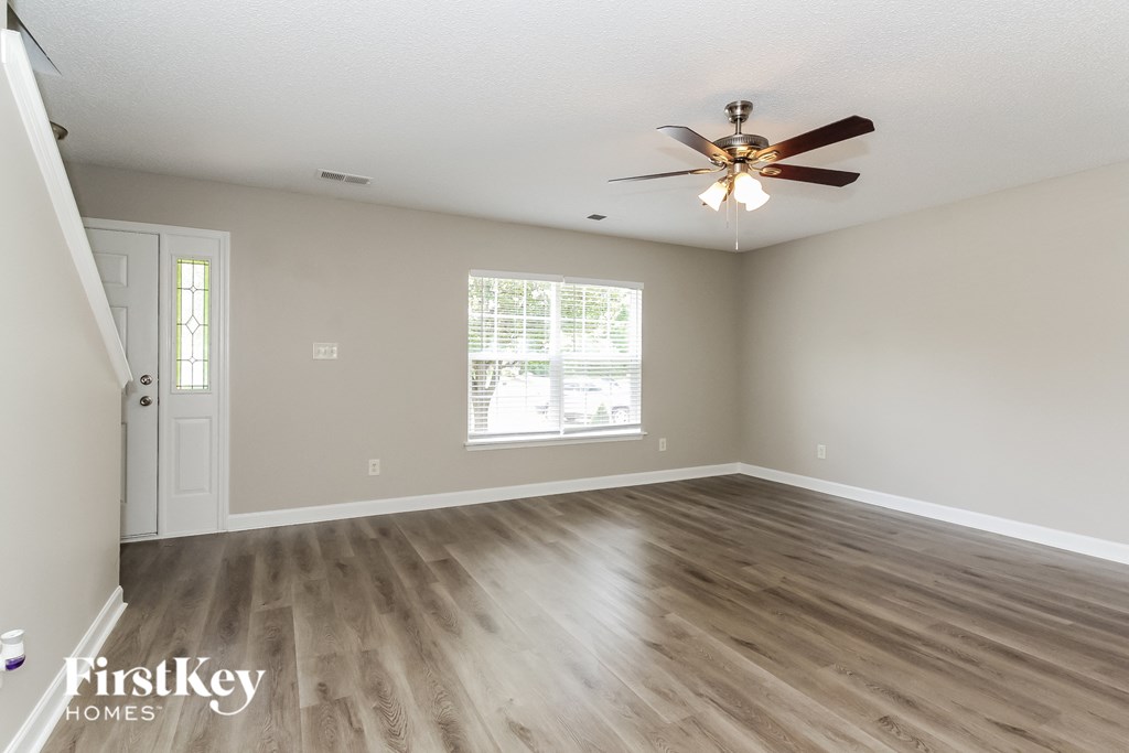 the spacious living room with hardwood flooring and a ceiling fan
