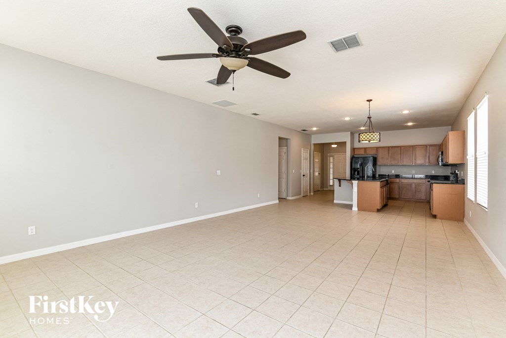 A spacious empty room with a ceiling fan and a kitchen area in the background.