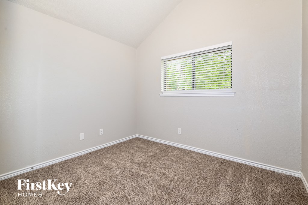 the bedroom of a small house with carpet and a window