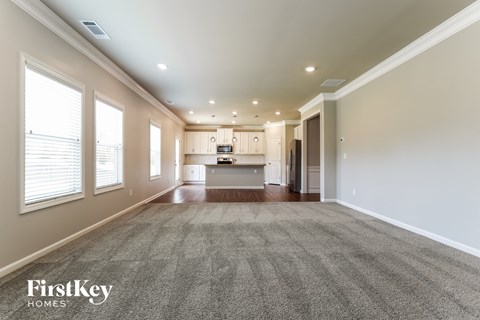 an empty living room with a kitchen in the background