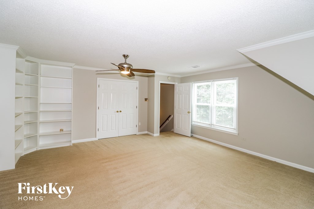an empty living room with a ceiling fan and white shelves