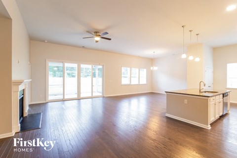 an empty living room with a kitchen and a ceiling fan