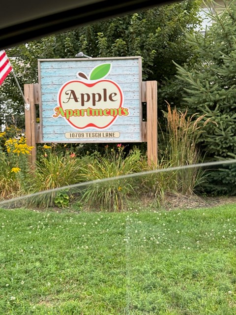 A sign for Apple Apartments is displayed in front of a grassy area.