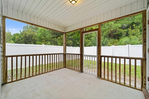 A white wooden porch with a white fence and trees in the background.