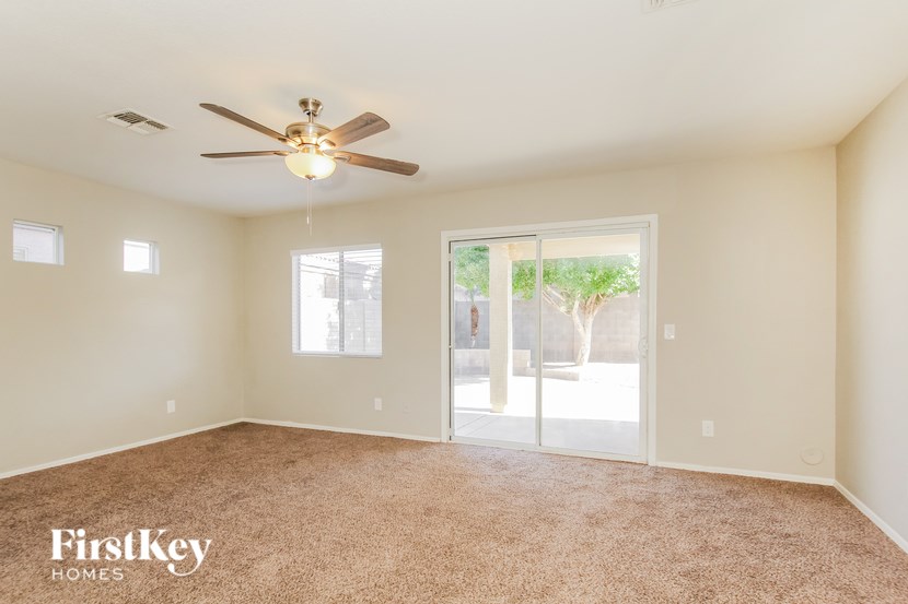 A spacious room with a carpeted floor, a ceiling fan, and a sliding glass door leading to a patio.