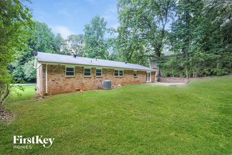 a small brick house with a green lawn and trees