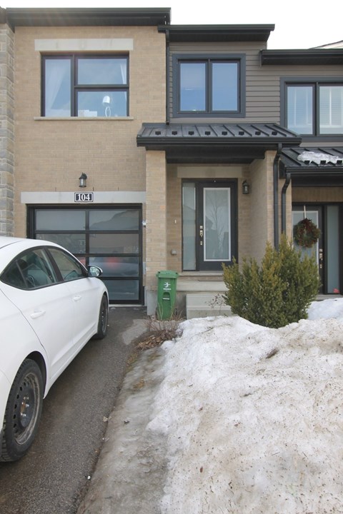 A white car is parked in front of a house with the number 8028 on the front.