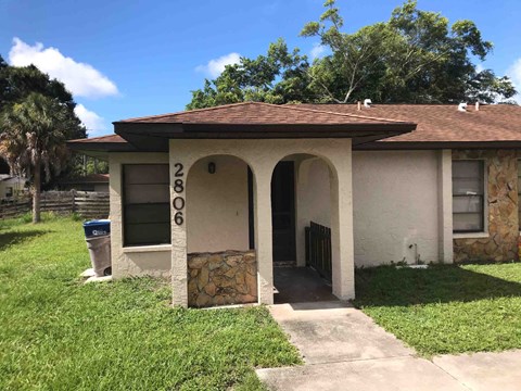 a small tan house with a driveway and a gate