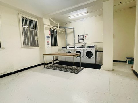 A laundry room with a washer and dryer, a table, and a metal grate on the floor.