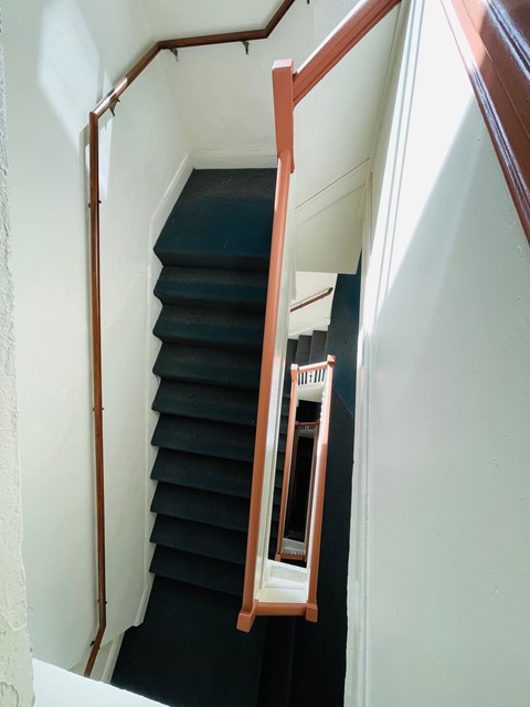 A staircase with a black carpet and wooden handrail.