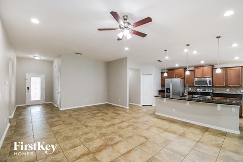 an empty living room with a kitchen and a ceiling fan