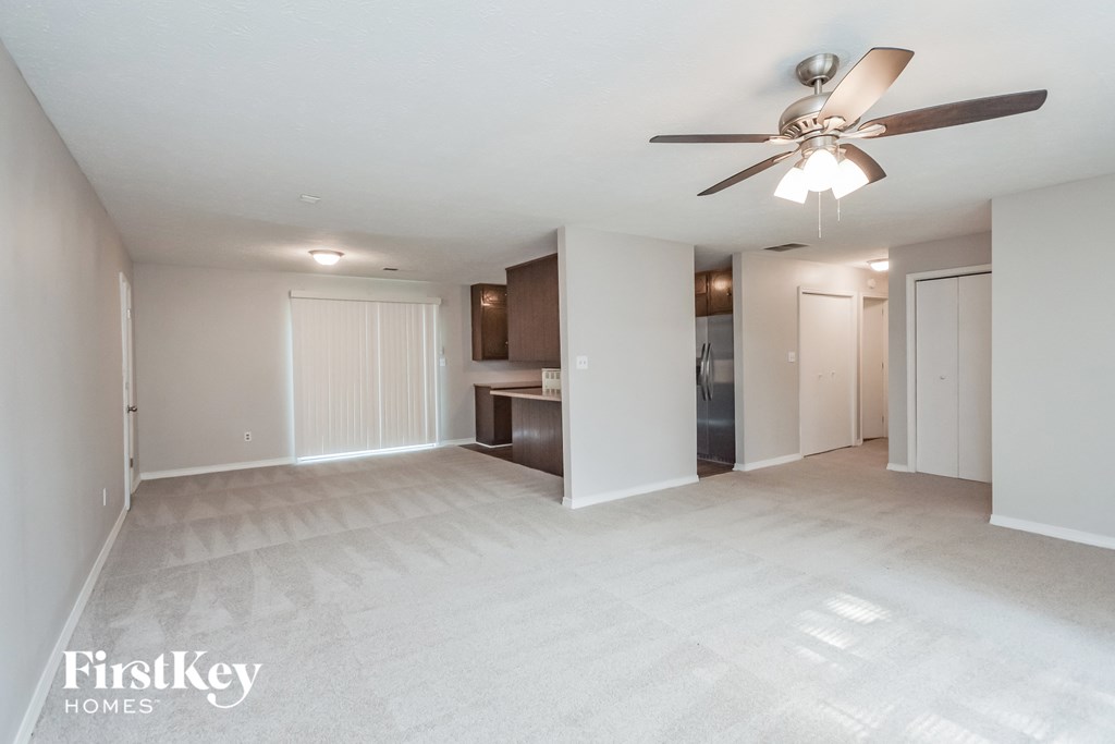 an empty living room with a ceiling fan and a kitchen