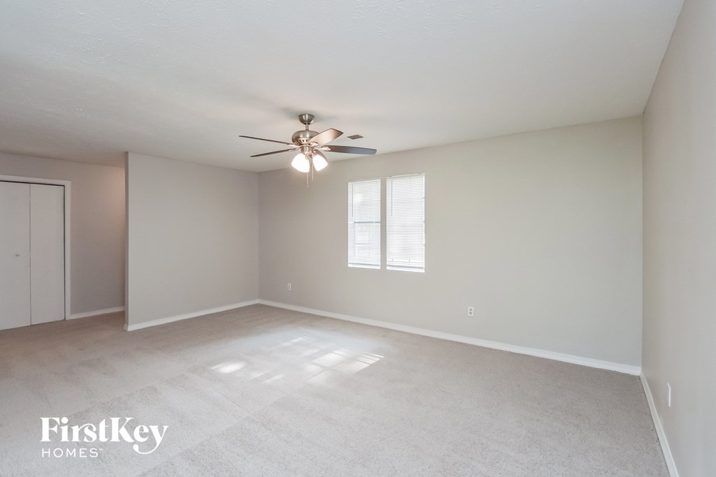 a spacious living room with white carpet and a ceiling fan