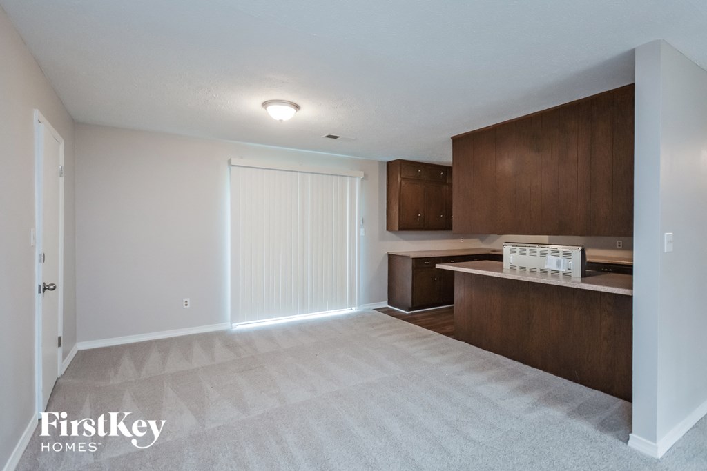 an empty living room and kitchen with wood cabinets and white carpet
