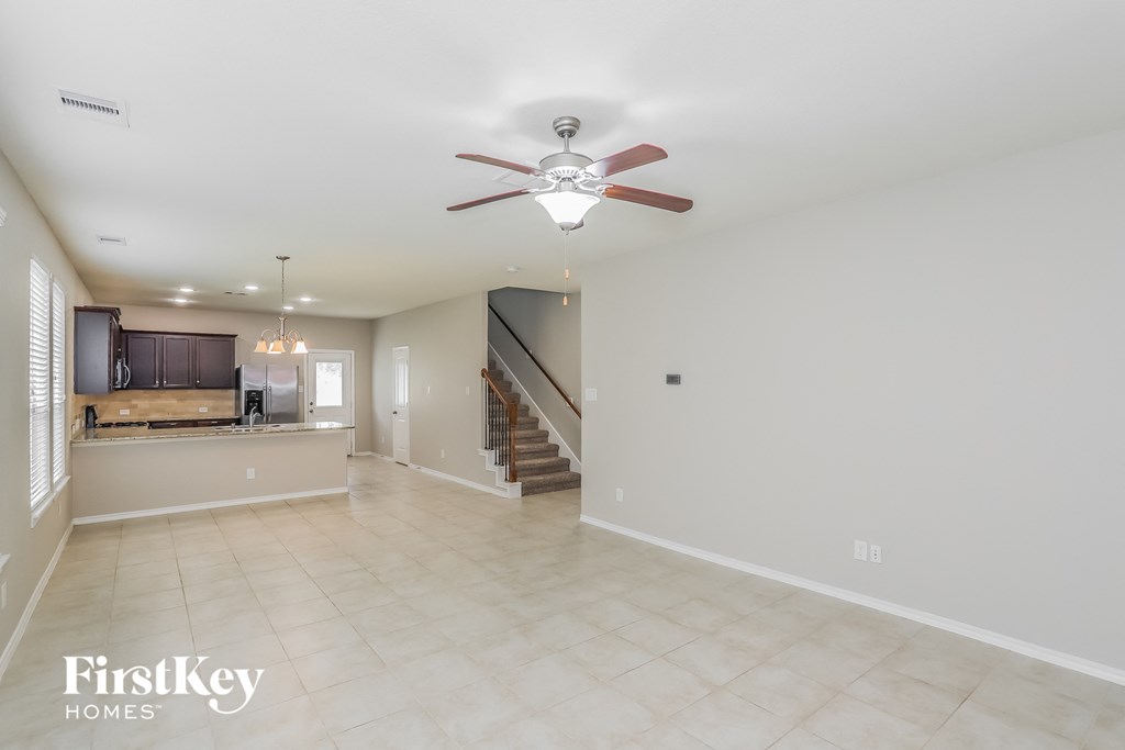 an empty living room with a ceiling fan and a kitchen