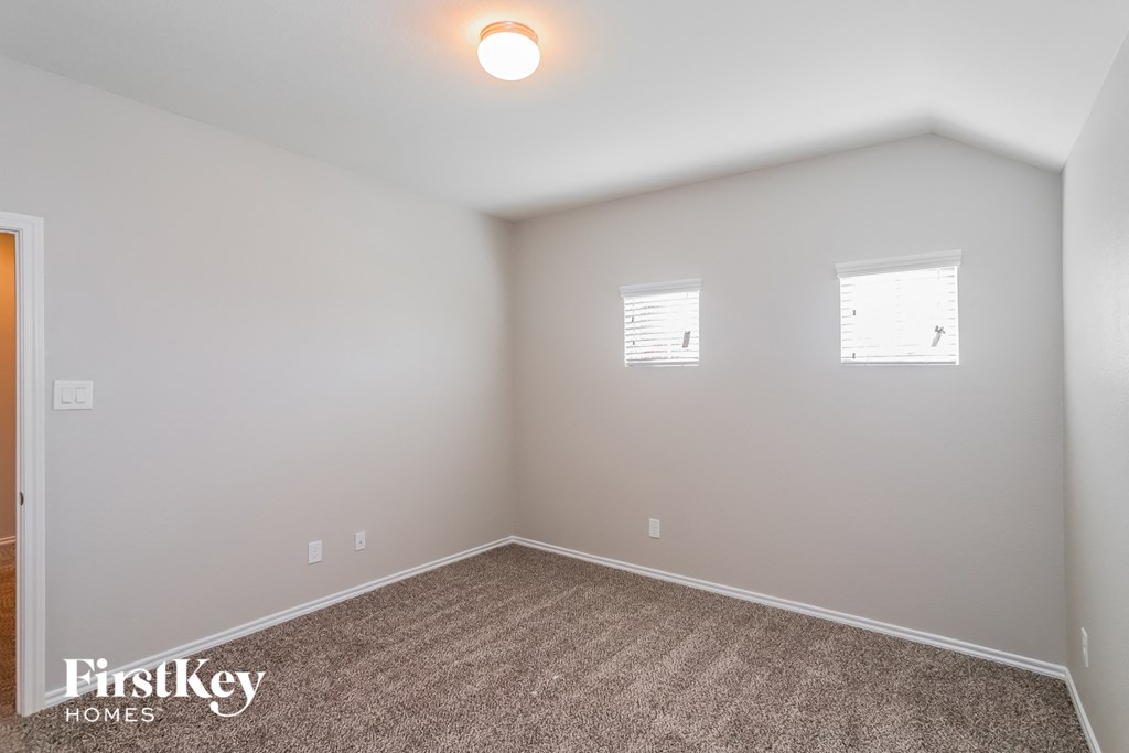 a bedroom with white walls and carpet and two windows