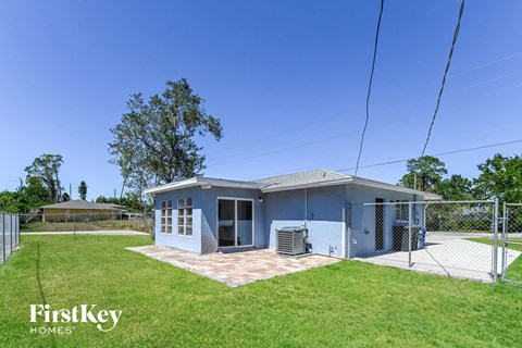 A blue house with a fence and trees in the background.