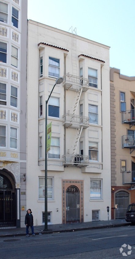 A person stands on a street in front of a white building with a fire escape.
