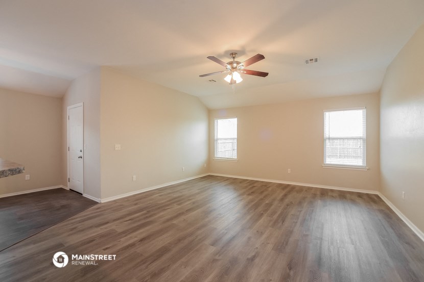 the spacious living room with hardwood floors and a ceiling fan