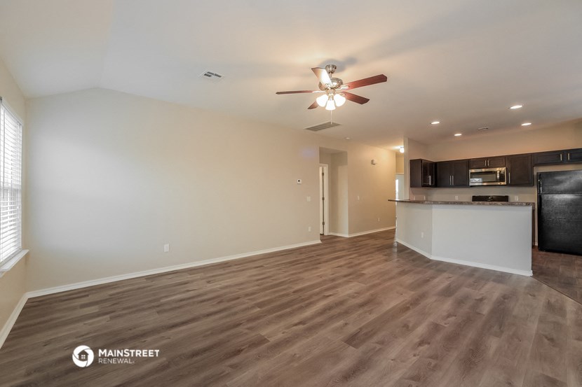 an empty living room with a ceiling fan and a kitchen