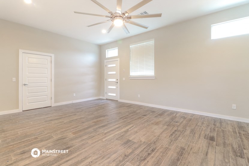 the spacious living room with wood flooring and a ceiling fan