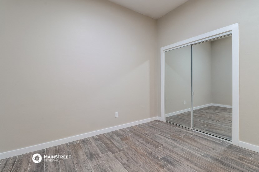 a bedroom with a mirrored closet and wood flooring