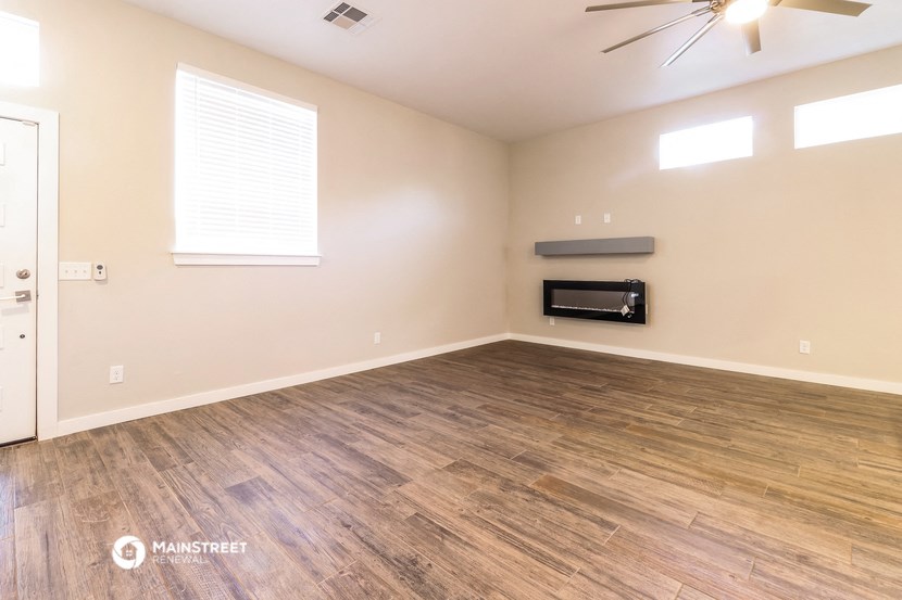 the spacious living room with hardwood flooring and a ceiling fan