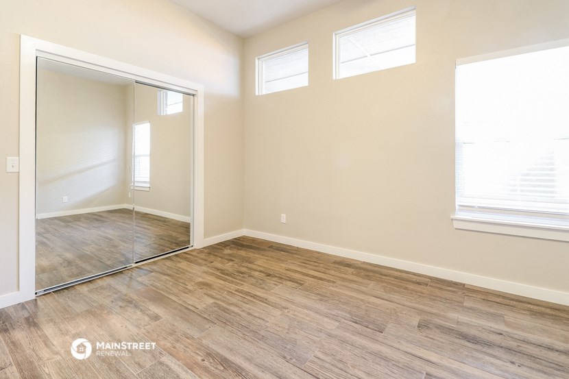 the living room of an empty home with wood flooring and a mirrored door
