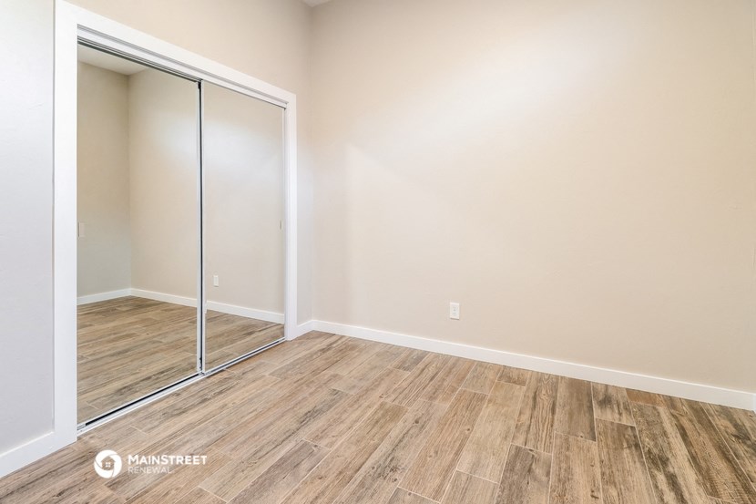 a bedroom with a mirrored closet door and wood flooring