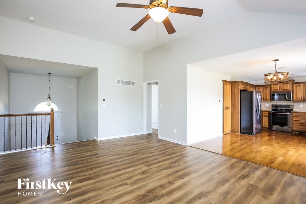 an empty living room with a kitchen and a ceiling fan