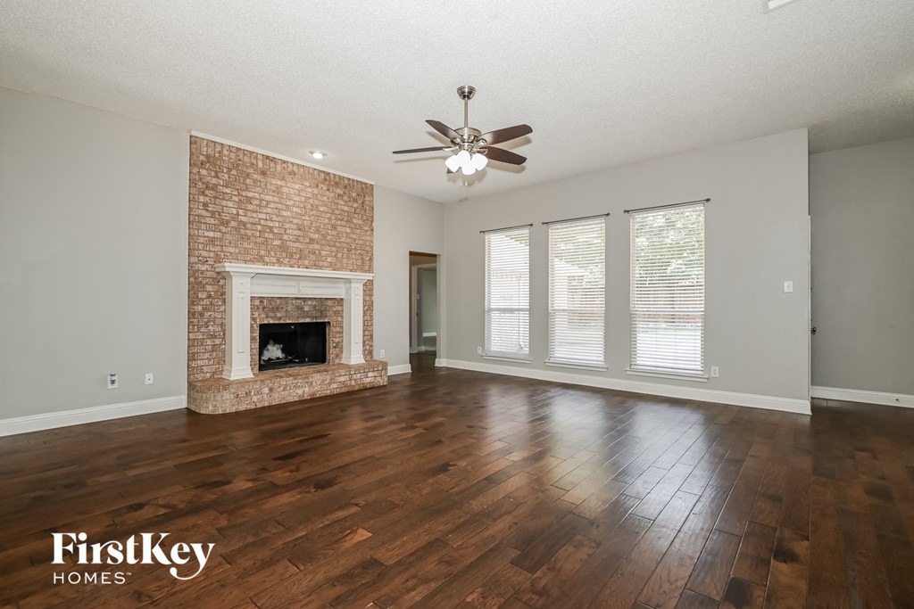 an empty living room with a brick fireplace and a ceiling fan