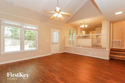 A spacious living room with wooden floors and a staircase in the background.