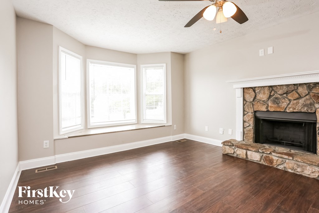 A living room with a stone fireplace and a ceiling fan.
