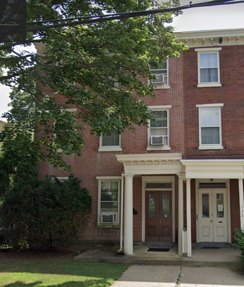 a brick building with a white door and a tree in front of it