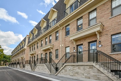 A row of red brick townhouses with black railings and white trim.