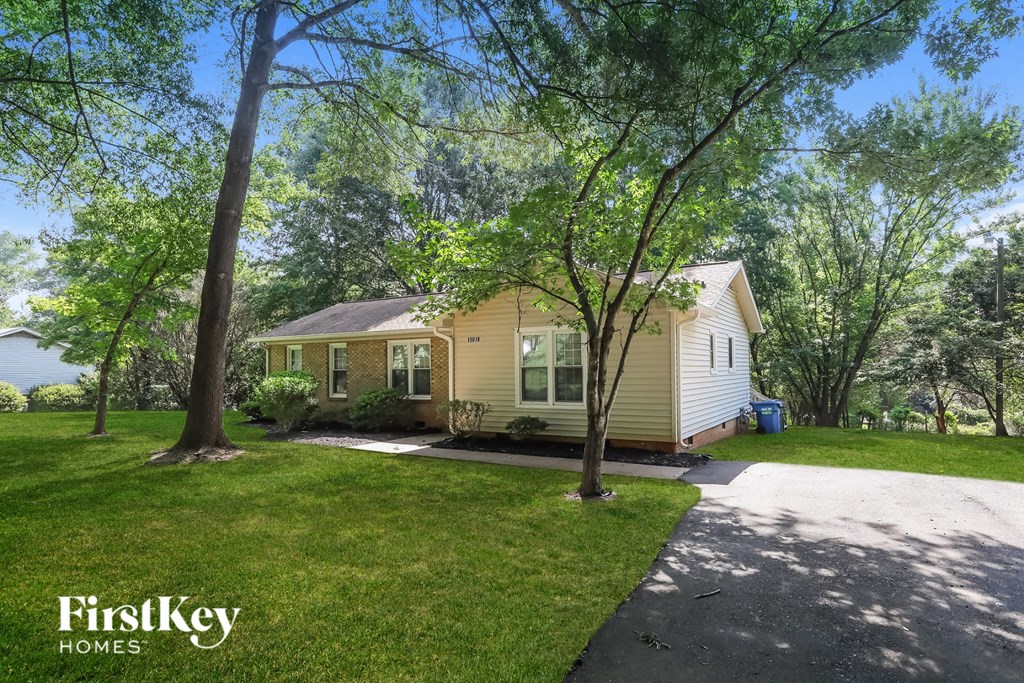 a small yellow house with a driveway and trees