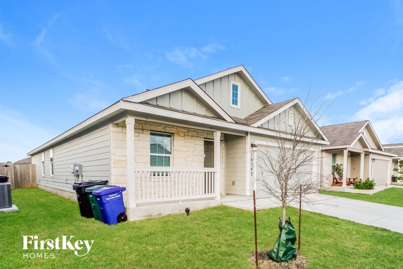 A house with a blue and green trash bin in front of it.
