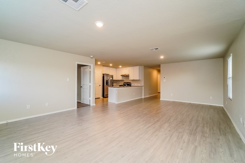 A spacious room with wooden flooring and a kitchen area in the background.