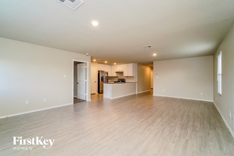 A spacious room with wooden flooring and a kitchen area in the background.