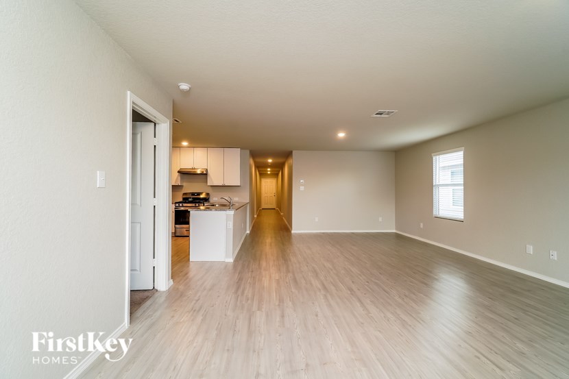 A spacious room with wooden flooring and a kitchen in the background.