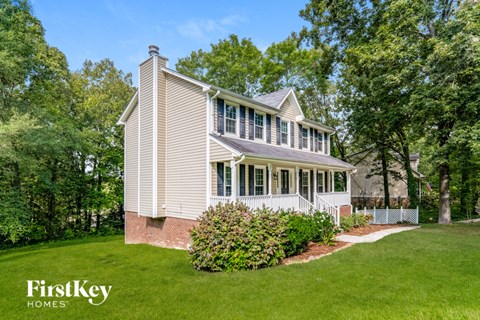 A house with a white porch and a brick chimney is surrounded by greenery.